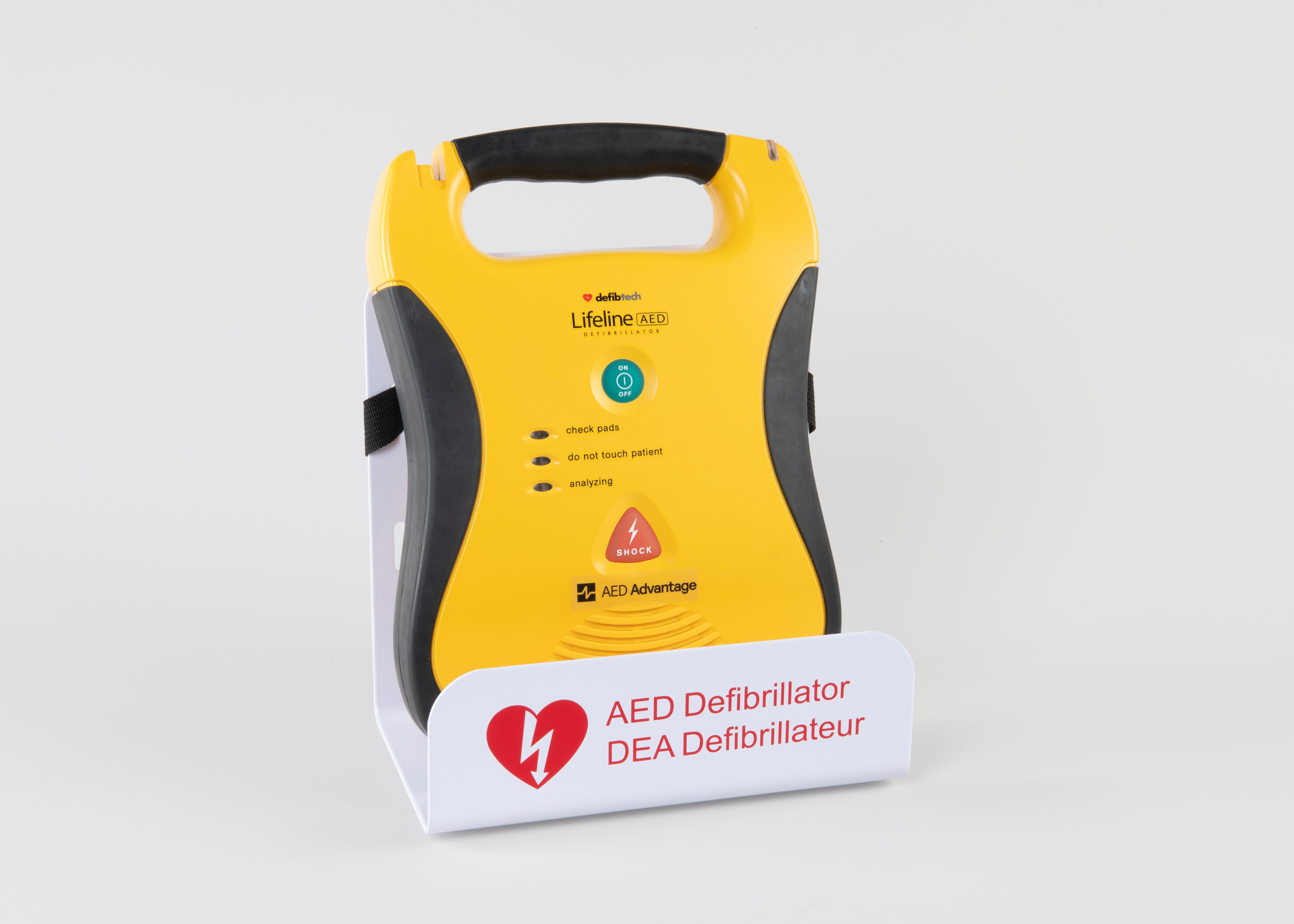 A black and yellow Lifeline AED displayed in a white metal wall mount bracket