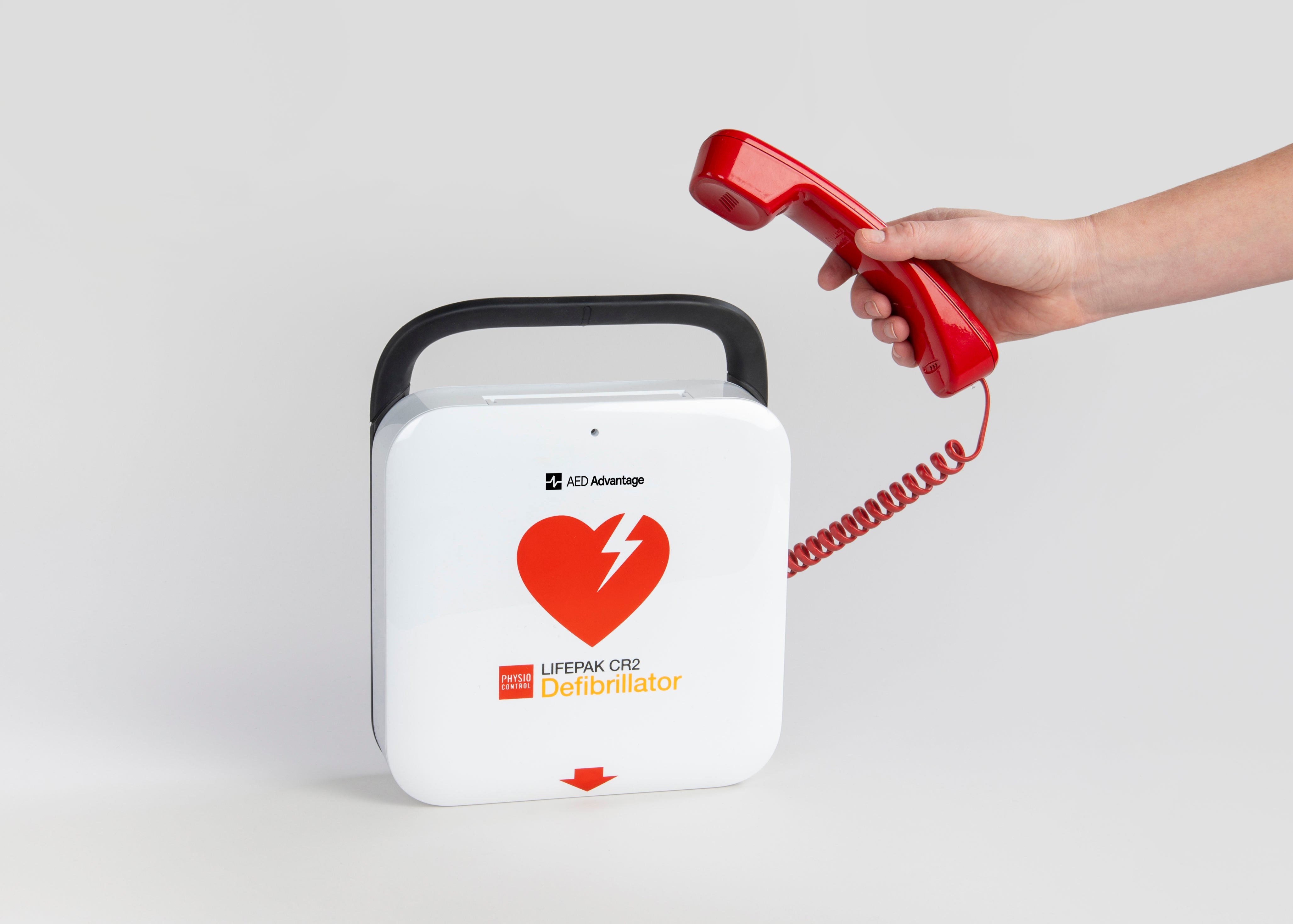 A white LIFEPAK CR2 AED and a hand holding a red phone.