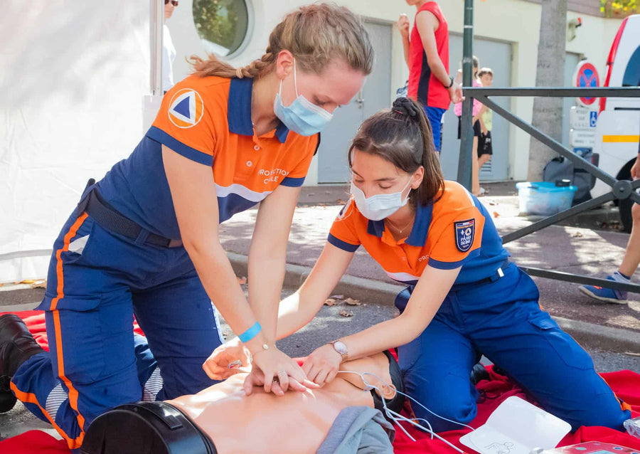 Two paramedics apply AED pads and perform CPR on a CPR dummy