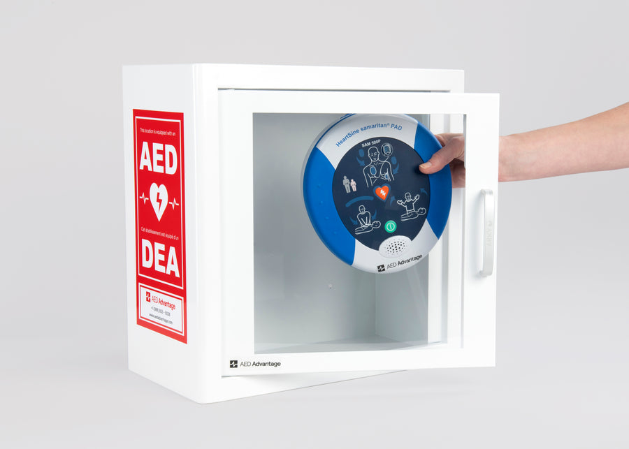 A blue and white HeartSine AED being retrieved by hand from a white metal cabinet with red decals