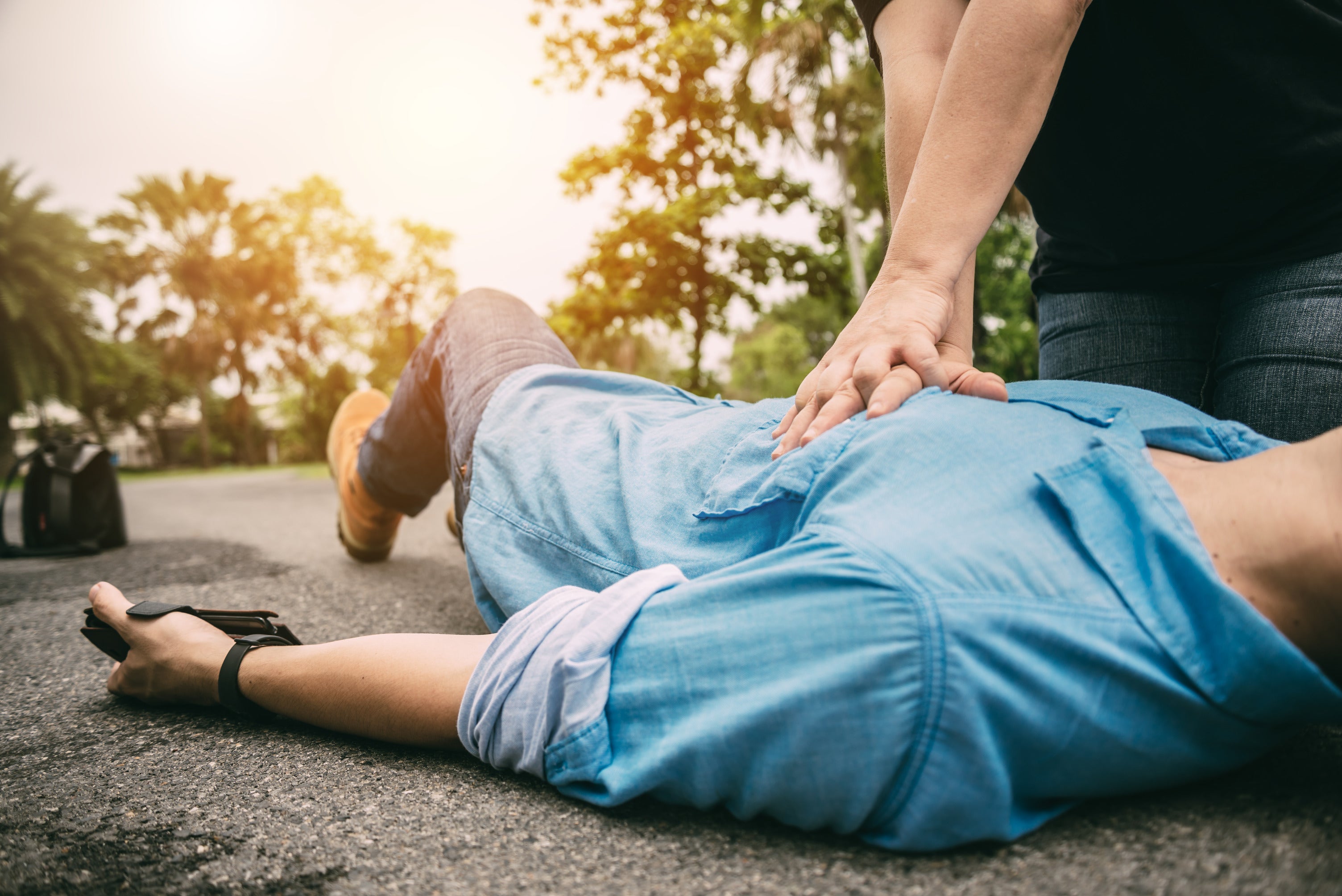 CPR compressions being delivered to an unconscious man in a blue shirt