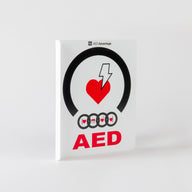 A white plastic rectangular wall sign containing large bold text indicating an AED is present 