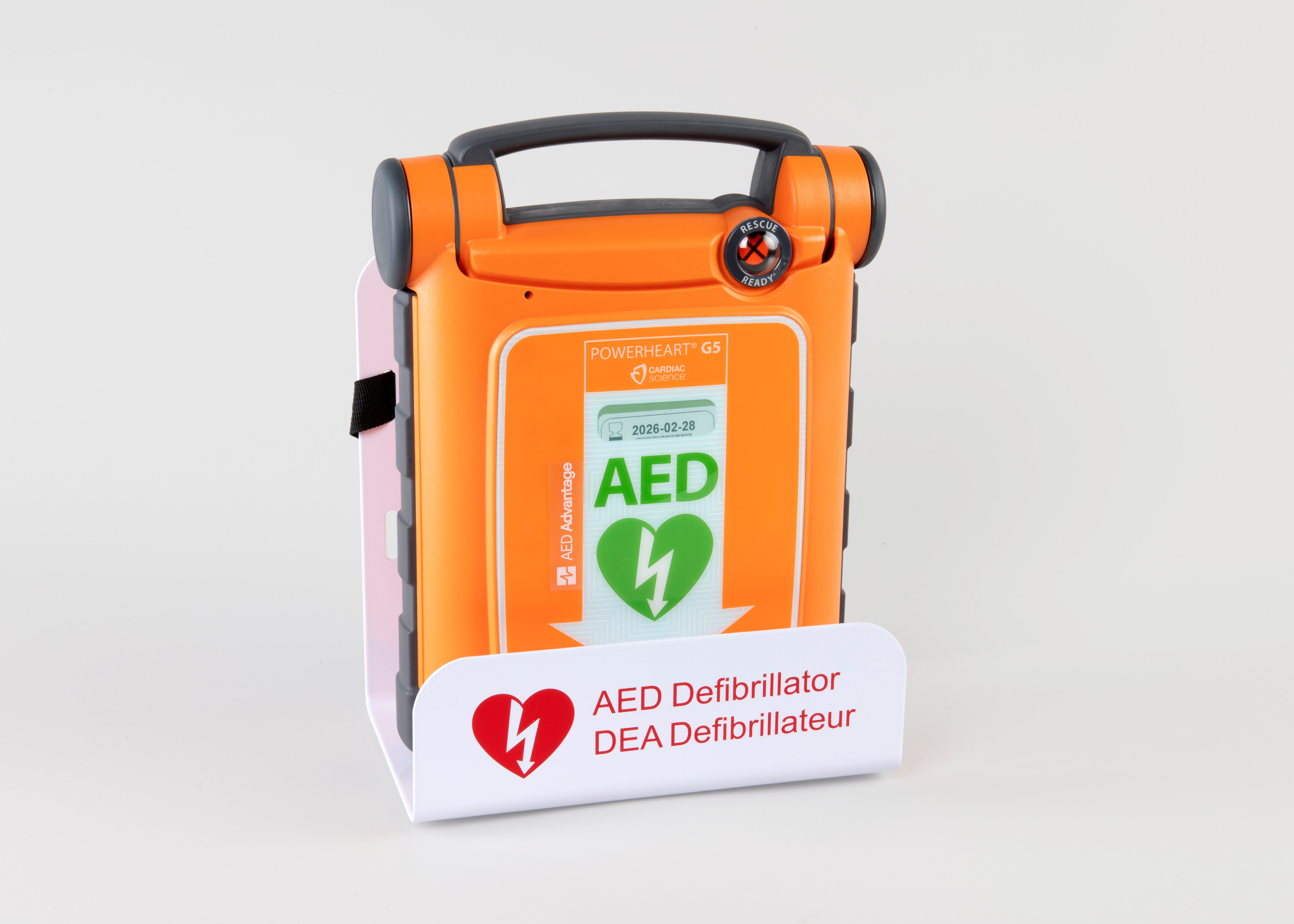 An orange Powerheart G5 AED displayed in a white metal wall mount bracket.