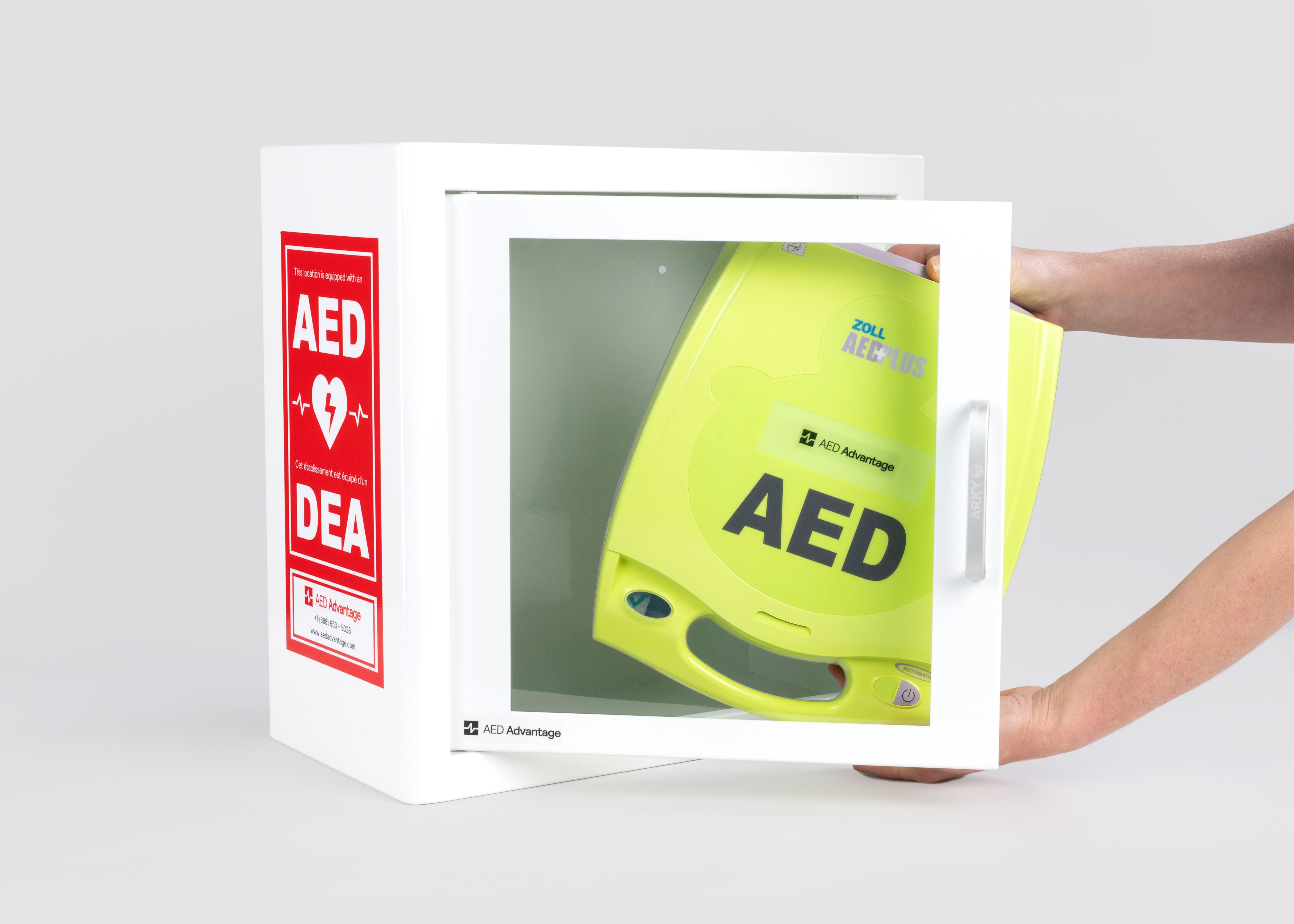 A green ZOLL AED plus machine being retrieved by hand from a white metal cabinet with red decals