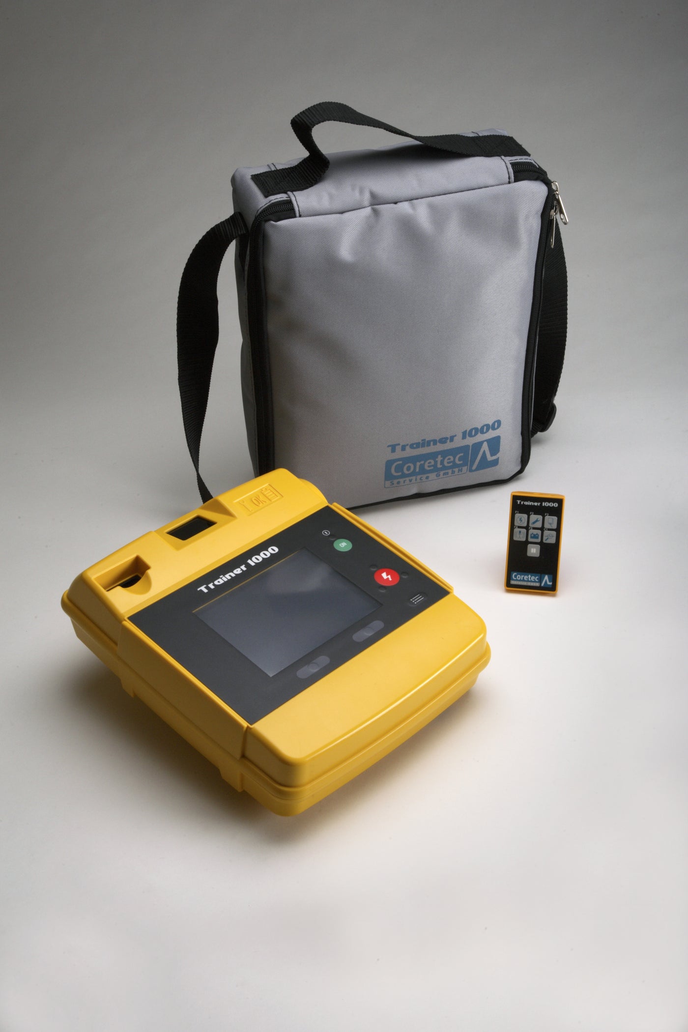 A yellow LIFEPAK 1000 training AED, its remote, and gray carry bag